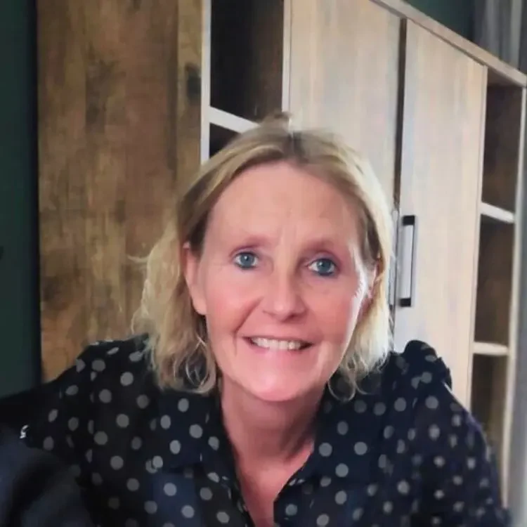Jolanda, oprichter van Saar’s Wonderweide, glimlacht vriendelijk in een huiselijke setting met houten kast op de achtergrond