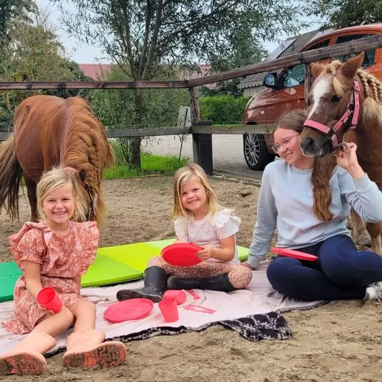 2 meisjes en een dame aan het picknicken met pony's
